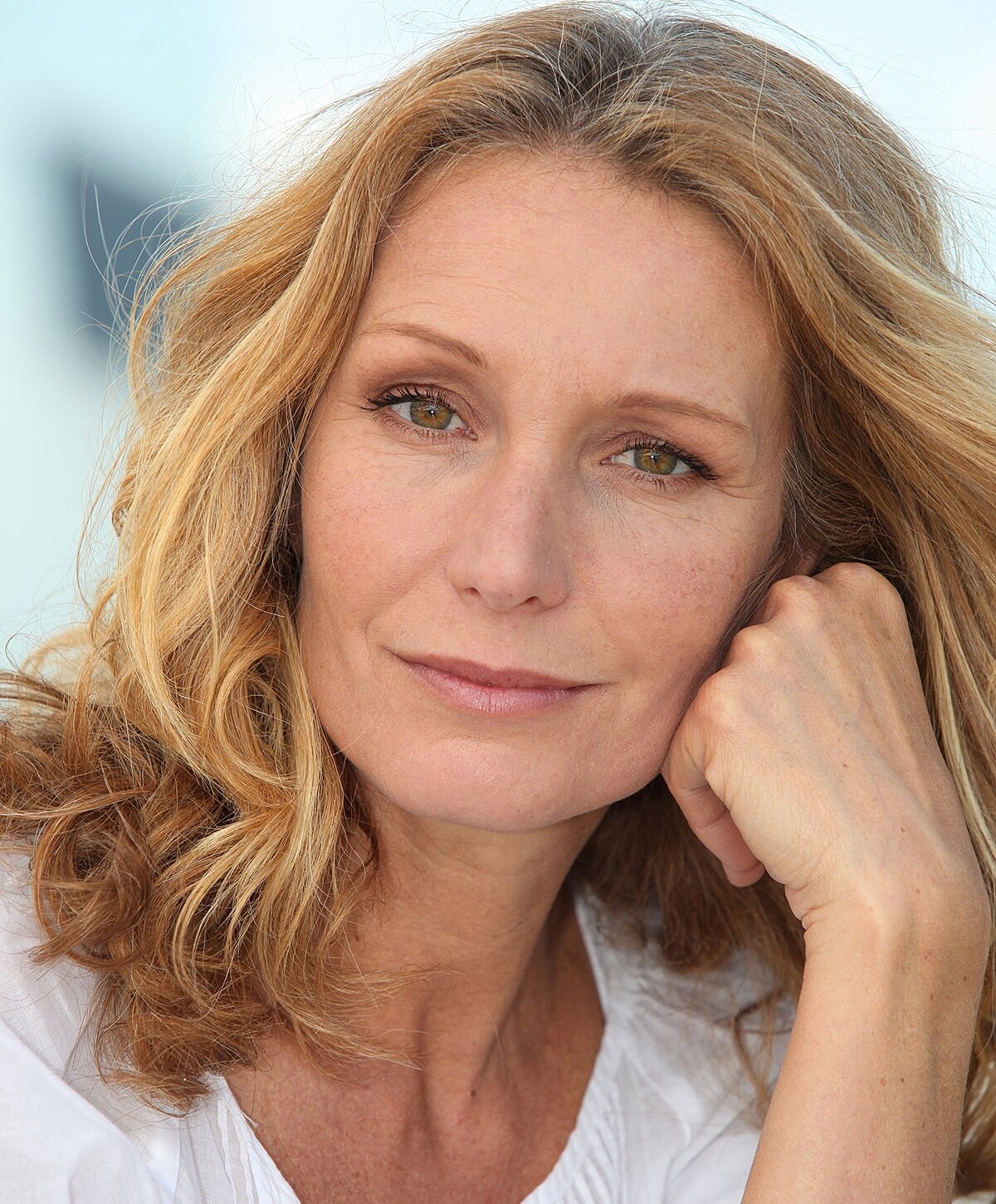 Woman with wavy hair resting chin on hand