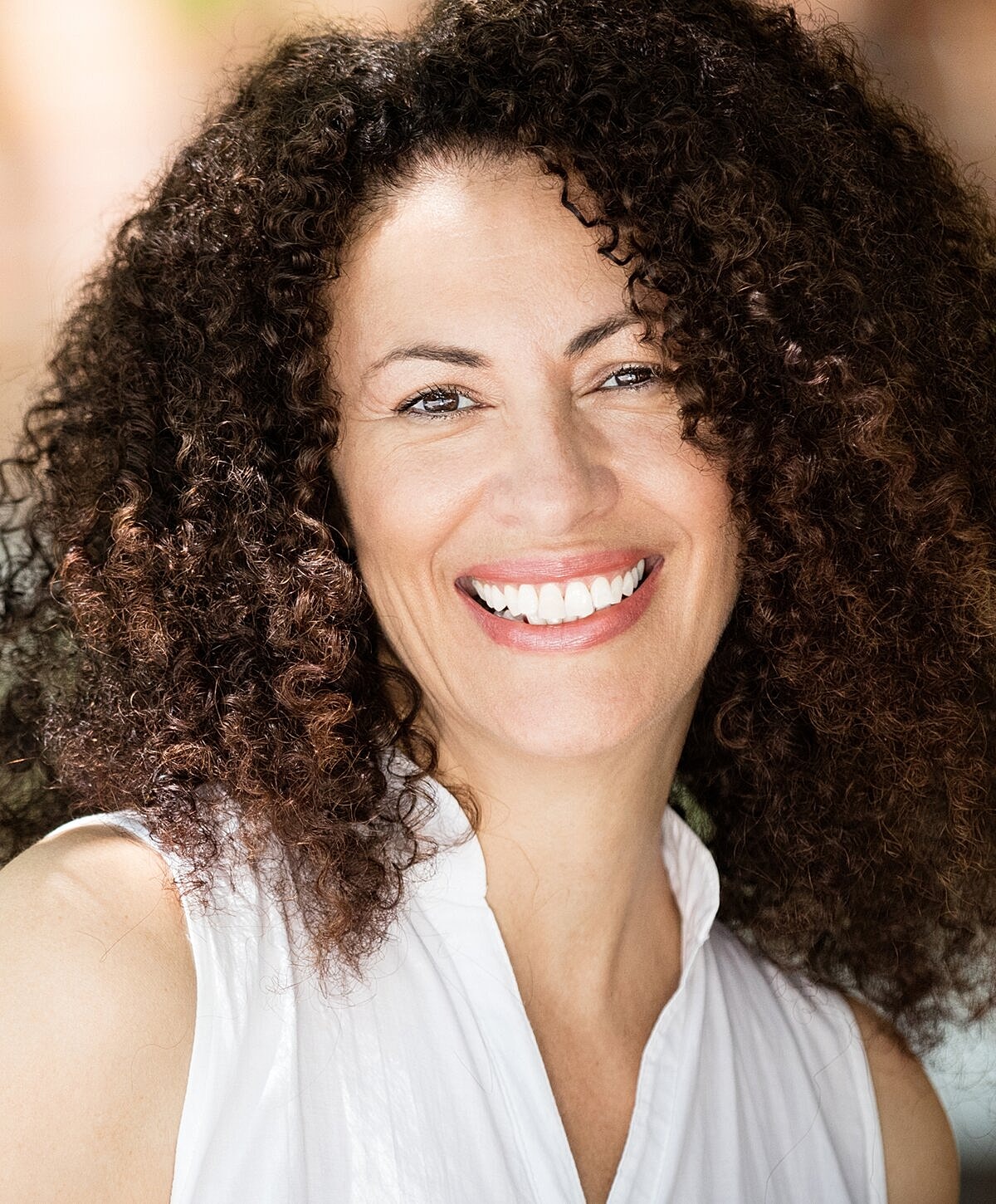 Smiling woman with curly hair in white shirt.