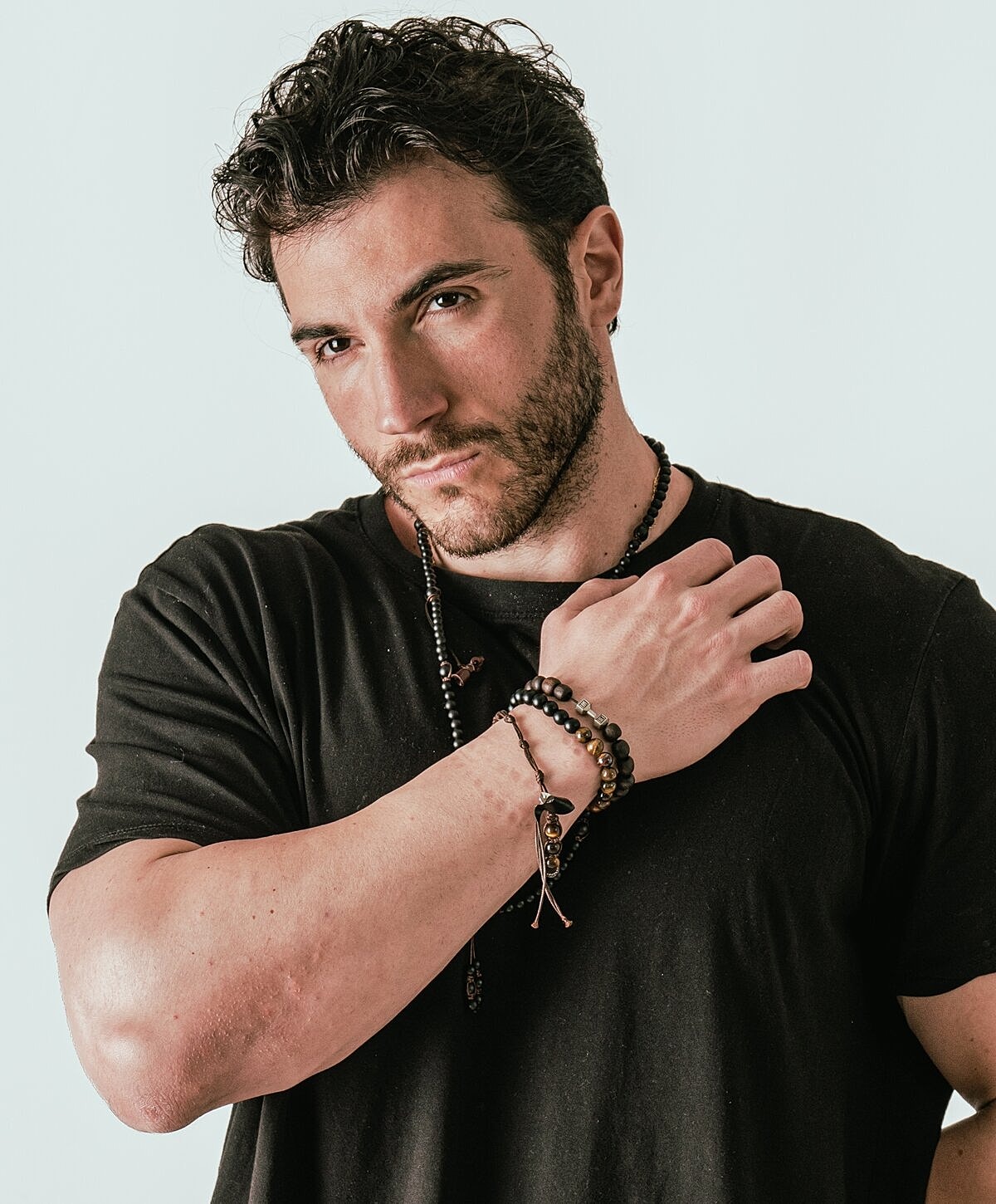 Man in black shirt with bracelets posing confidently.