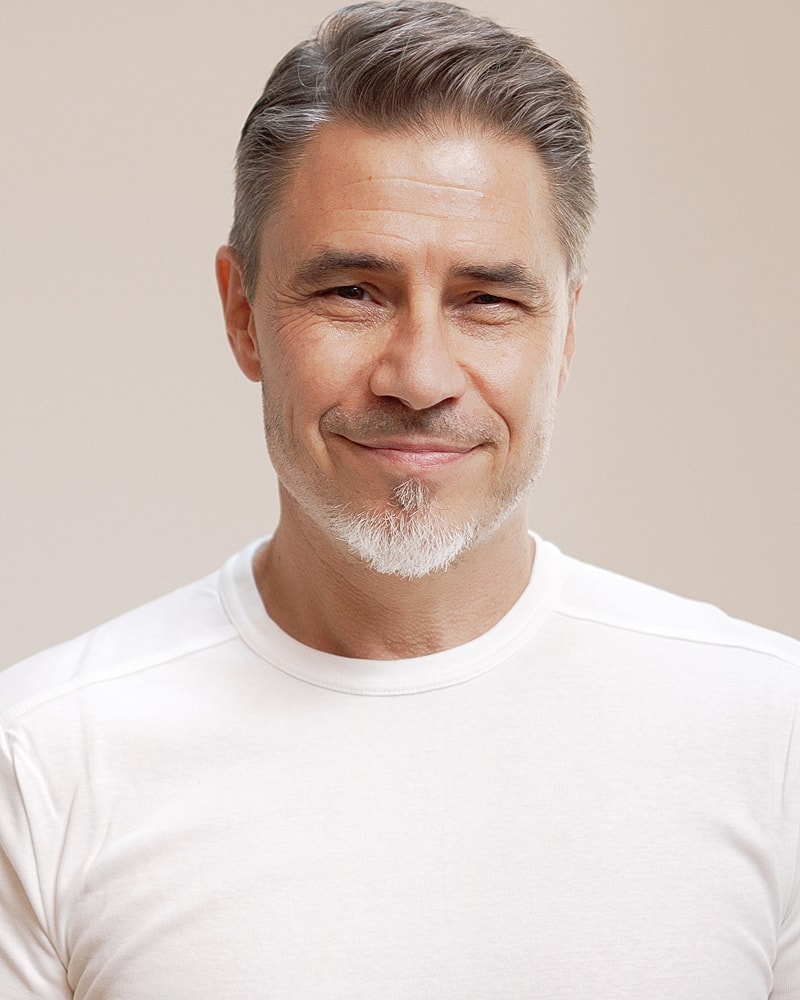 Smiling man in a white shirt against beige background.
