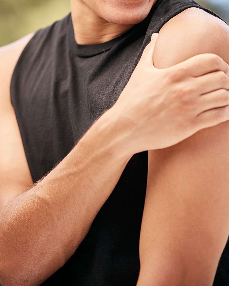 Person touching their shoulder in sleeveless shirt.