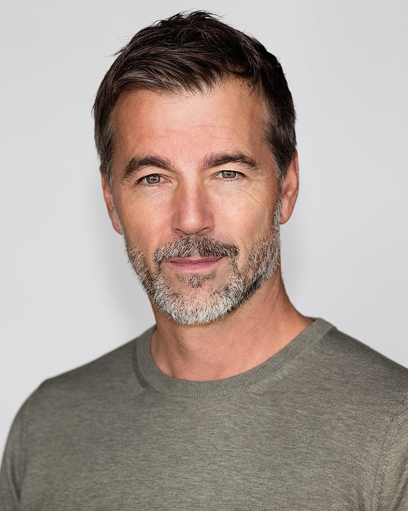 Man with beard, smiling in casual attire.