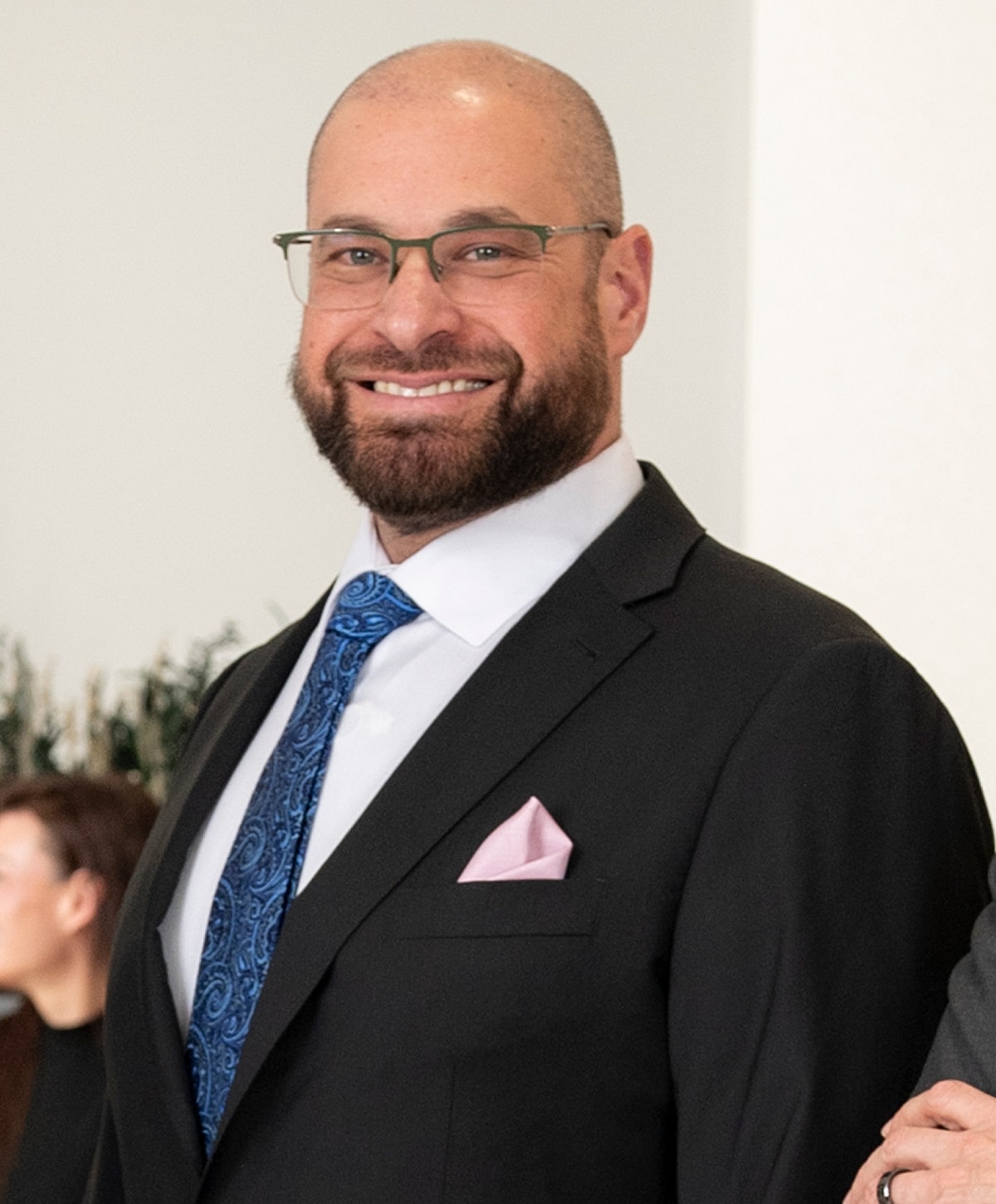 Man in suit with glasses and beard smiling.