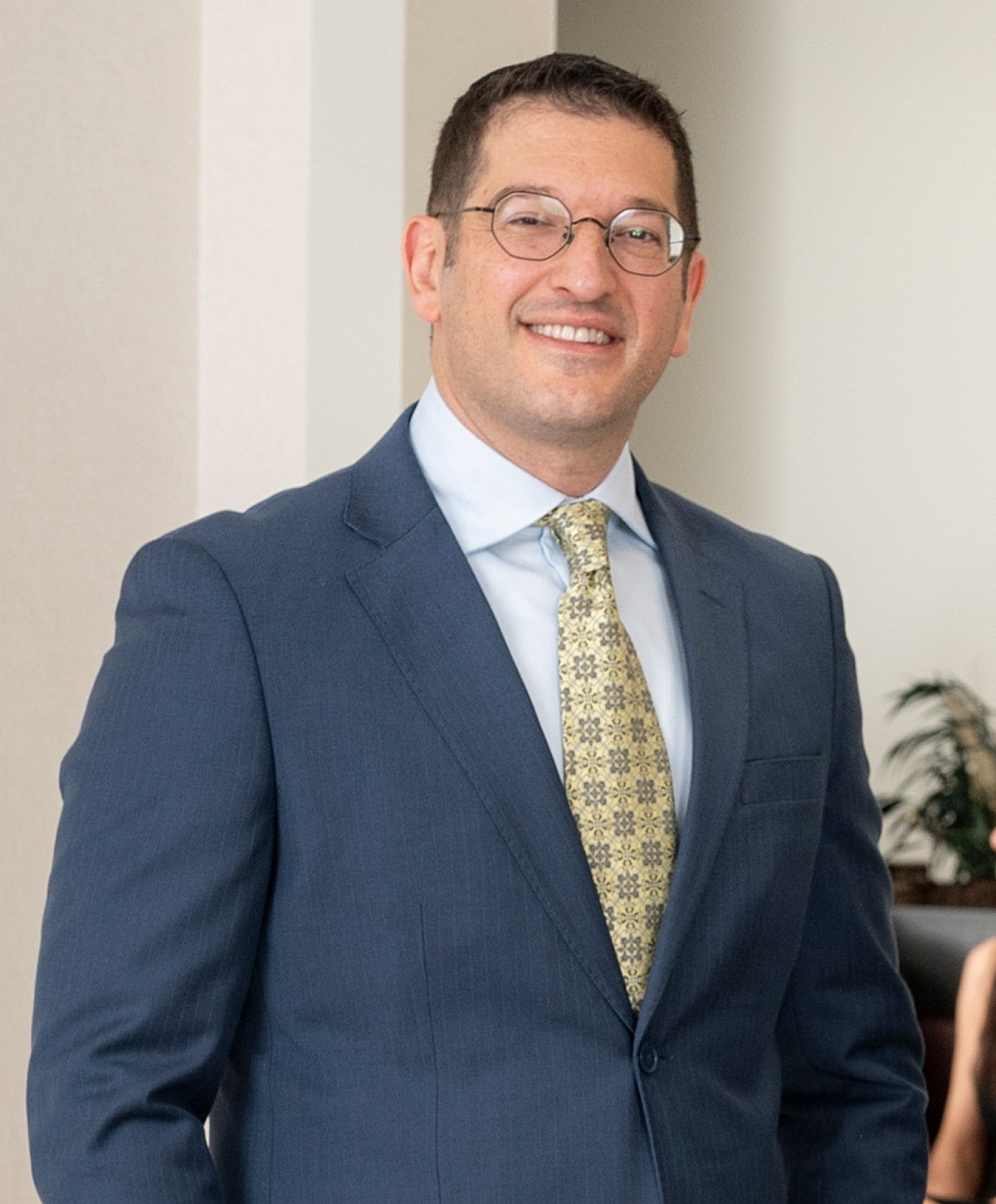 Man in a suit and glasses smiling confidently.