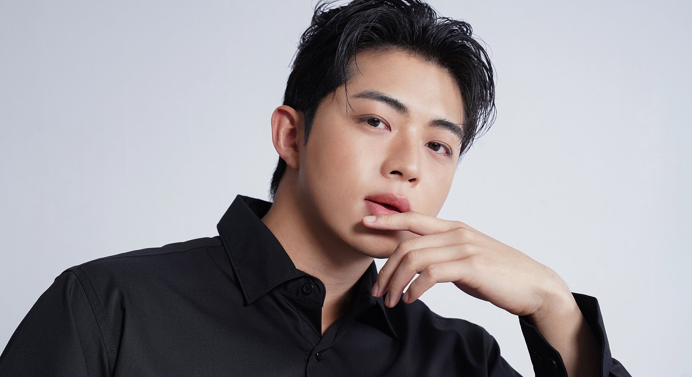 Young man in black shirt, posing thoughtfully.