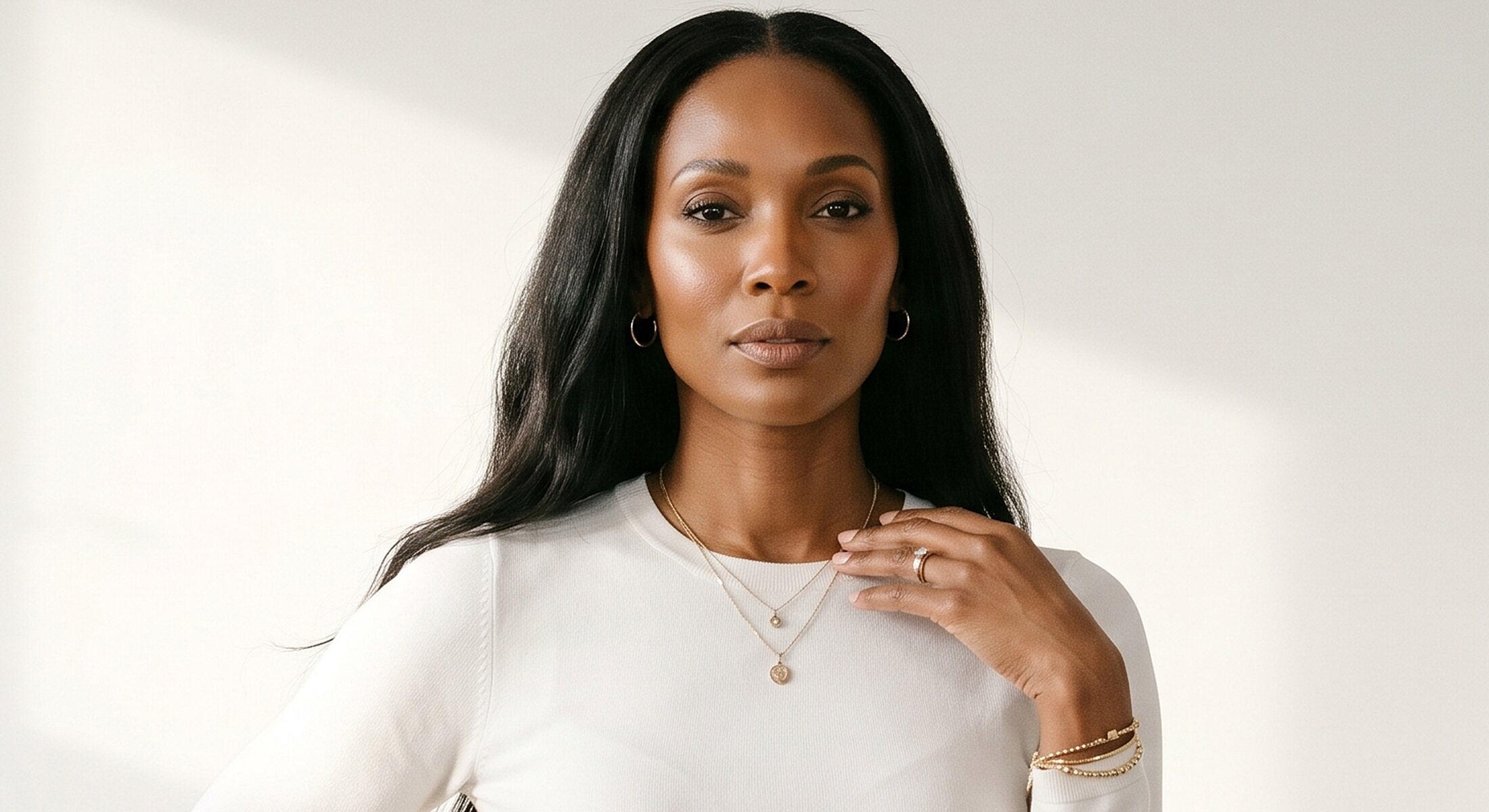 Woman with long hair in white top and jewelry.