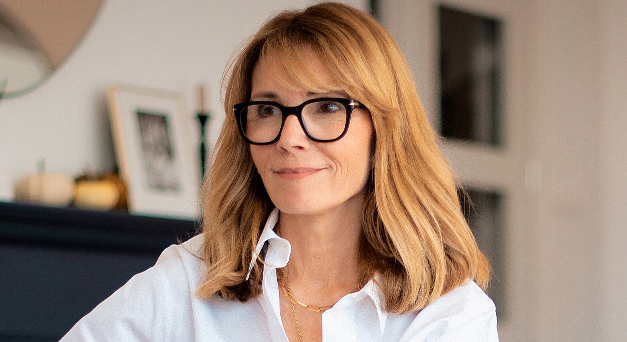 Woman with glasses smiling indoors.